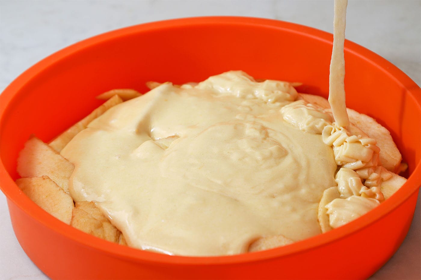 making-charlotte-apple-pie-pouring-the-batter-into-the-cake-pan-on-top-of-the-apples-2