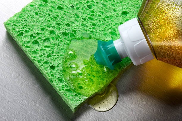 macro-shot-of-dish-soap-being-squeezed-onto-green-sponge-in-aluminum-sink-2